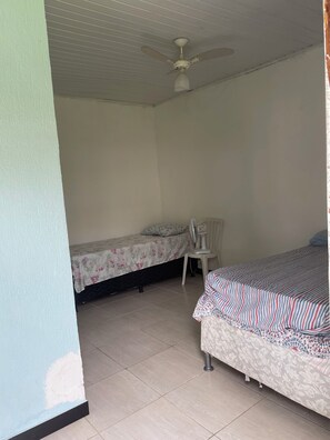 Een slaapkamer met twee bedden, een plafondventilator, een stoel en een betegelde vloer.