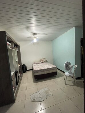 Een slaapkamer met een bed, een kledingkast, een plafondventilator en een stoel.