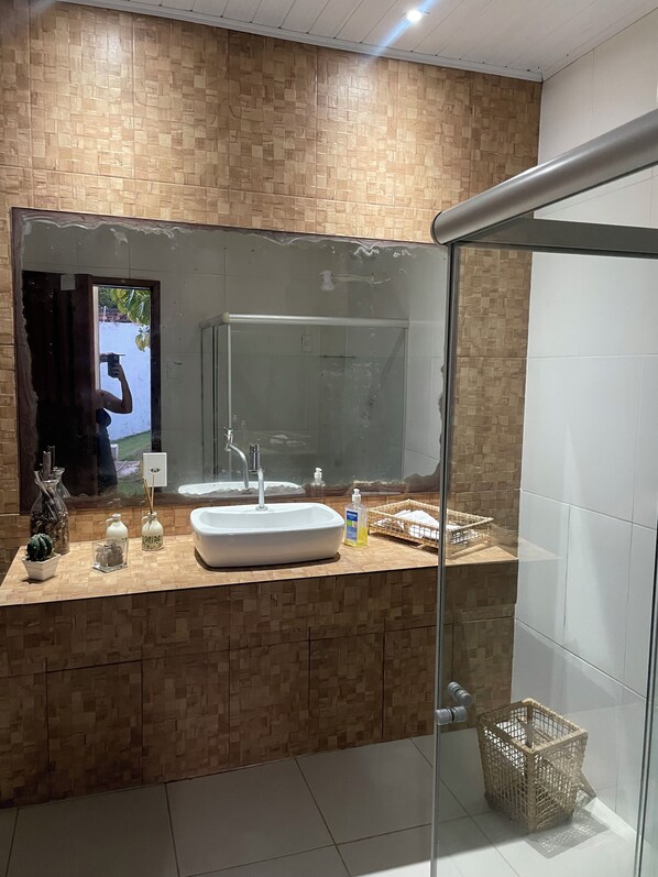 A modern bathroom with a wooden vanity, a large mirror, a glass shower enclosure, and a small wicker basket.