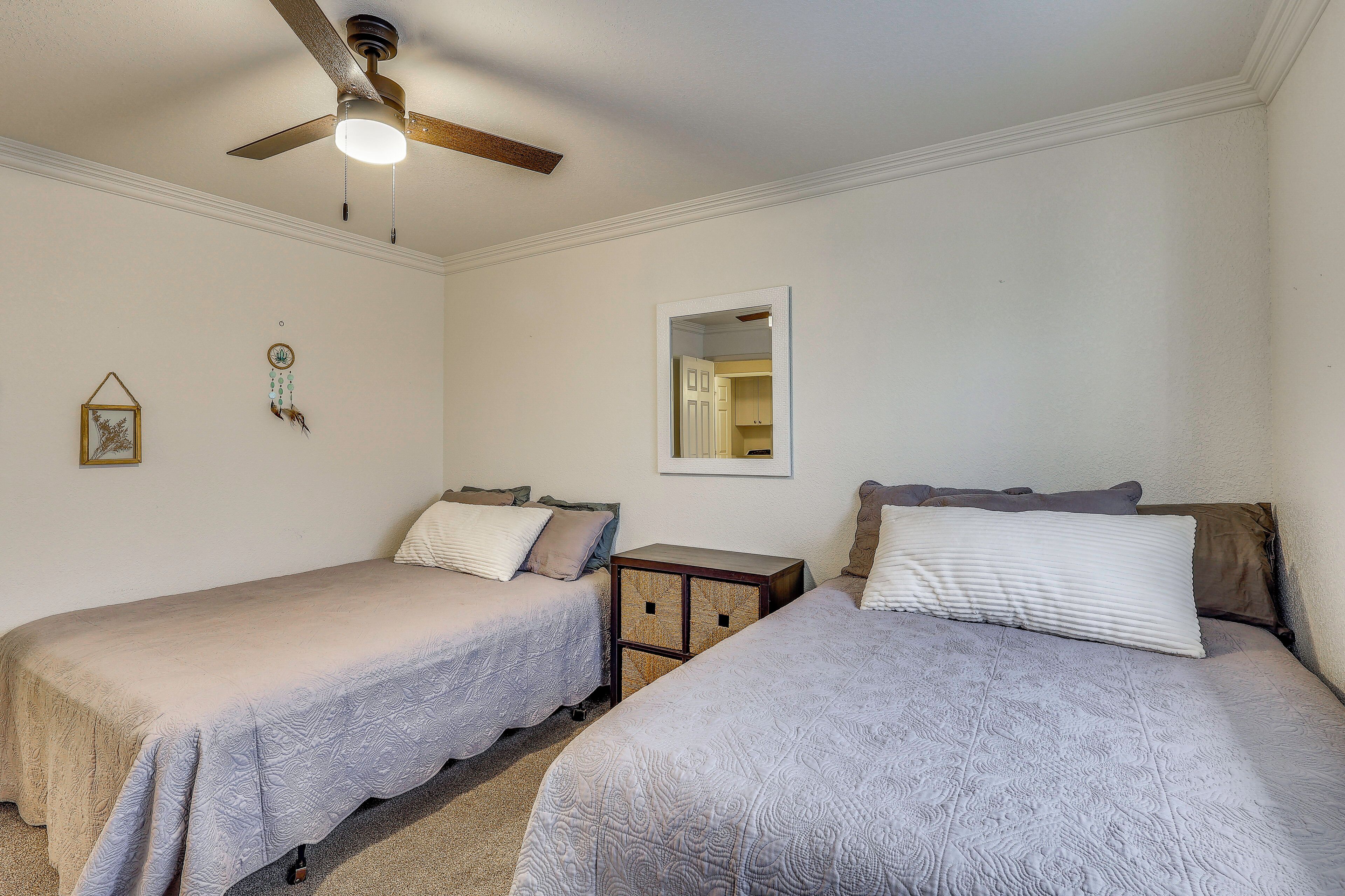 Ein Schlafzimmer mit zwei Einzelbetten, einem Deckenventilator, einem kleinen Nachttisch aus Holz und einem Spiegel an der Wand.