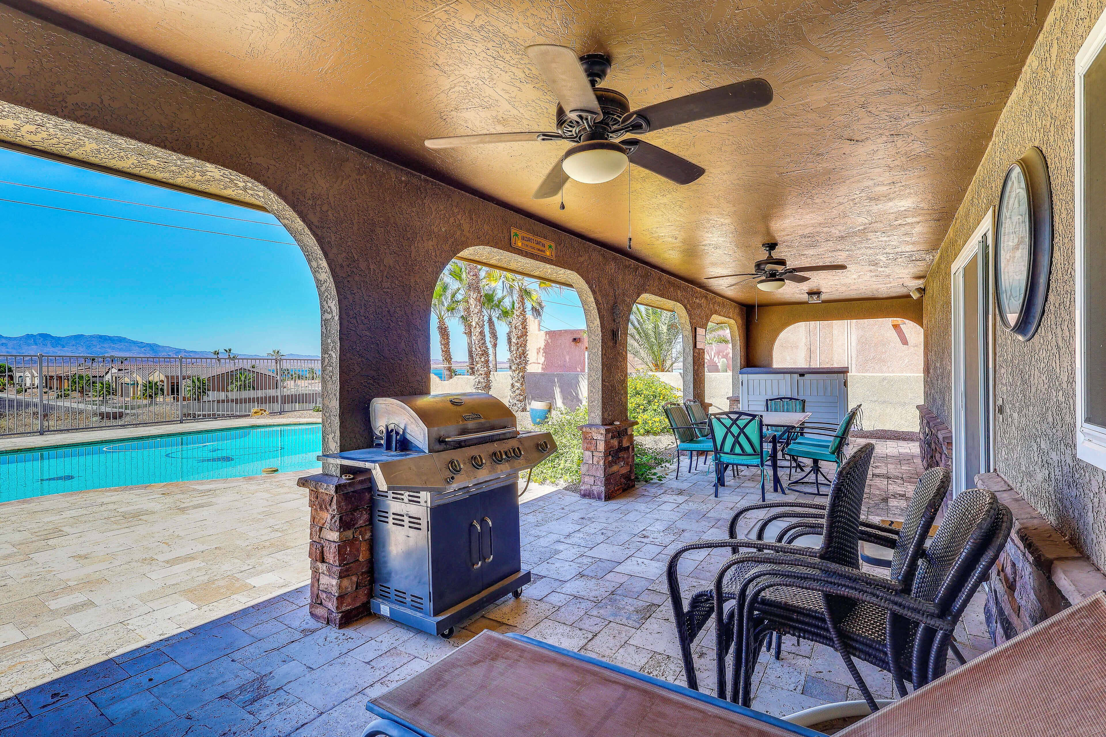 Eine Terrasse im Freien mit Pool, Grill, Korbmöbeln und Deckenventilator.