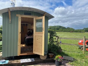 A small wooden cabin with a door open, revealing a bed and a window. - Shepherd Hut (Gloucester)