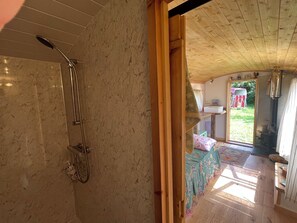 A wooden interior with a shower, a bed with a floral bedspread, and a view of the outdoors. - Shepherd Hut (Gloucester)