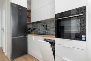 Eine moderne Küche mit einem schwarzen Kühlschrank, weißen Schränken, einer Holzarbeitsplatte, einem Geschirrspüler und einem schwarzen Backofen mit einem backsplash in Blattform.