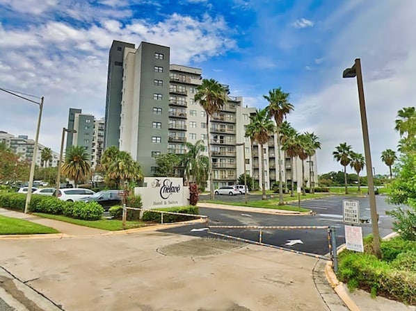 Entrada de hotel com uma placa, palmeiras e um edifício alto ao fundo.
