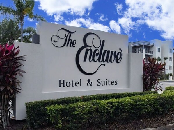 Ein Schild für 'The Enclave Hotel & Suites' mit einem modernen Gebäude im Hintergrund.