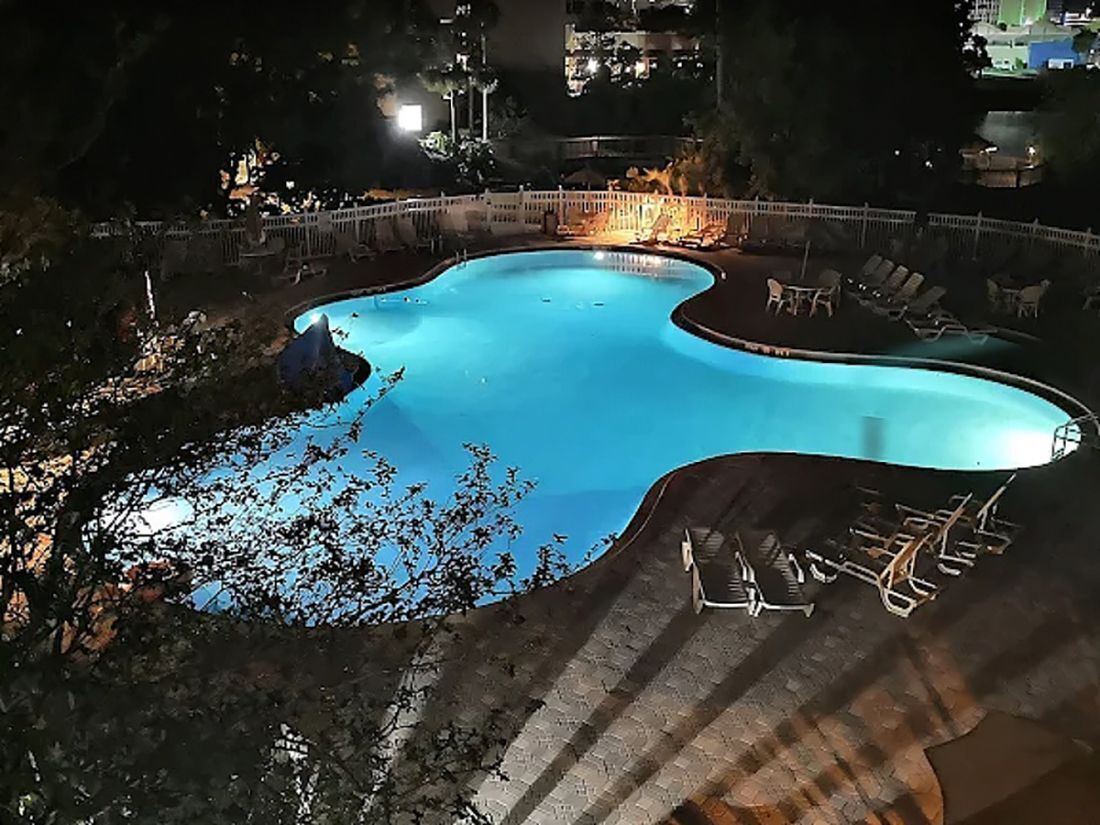 A swimming pool with a curved edge, surrounded by a white fence and lounge chairs.