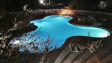A swimming pool with a curved edge, surrounded by a white fence and lounge chairs.