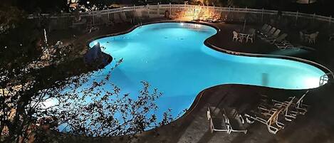 A swimming pool with a curved edge, surrounded by a white fence and lounge chairs.