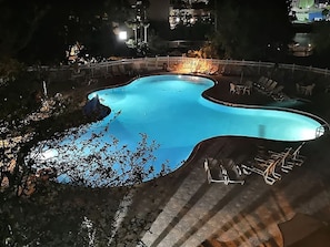 Piscina com borda curva, cercada por um muro branco e cadeiras de descanso.