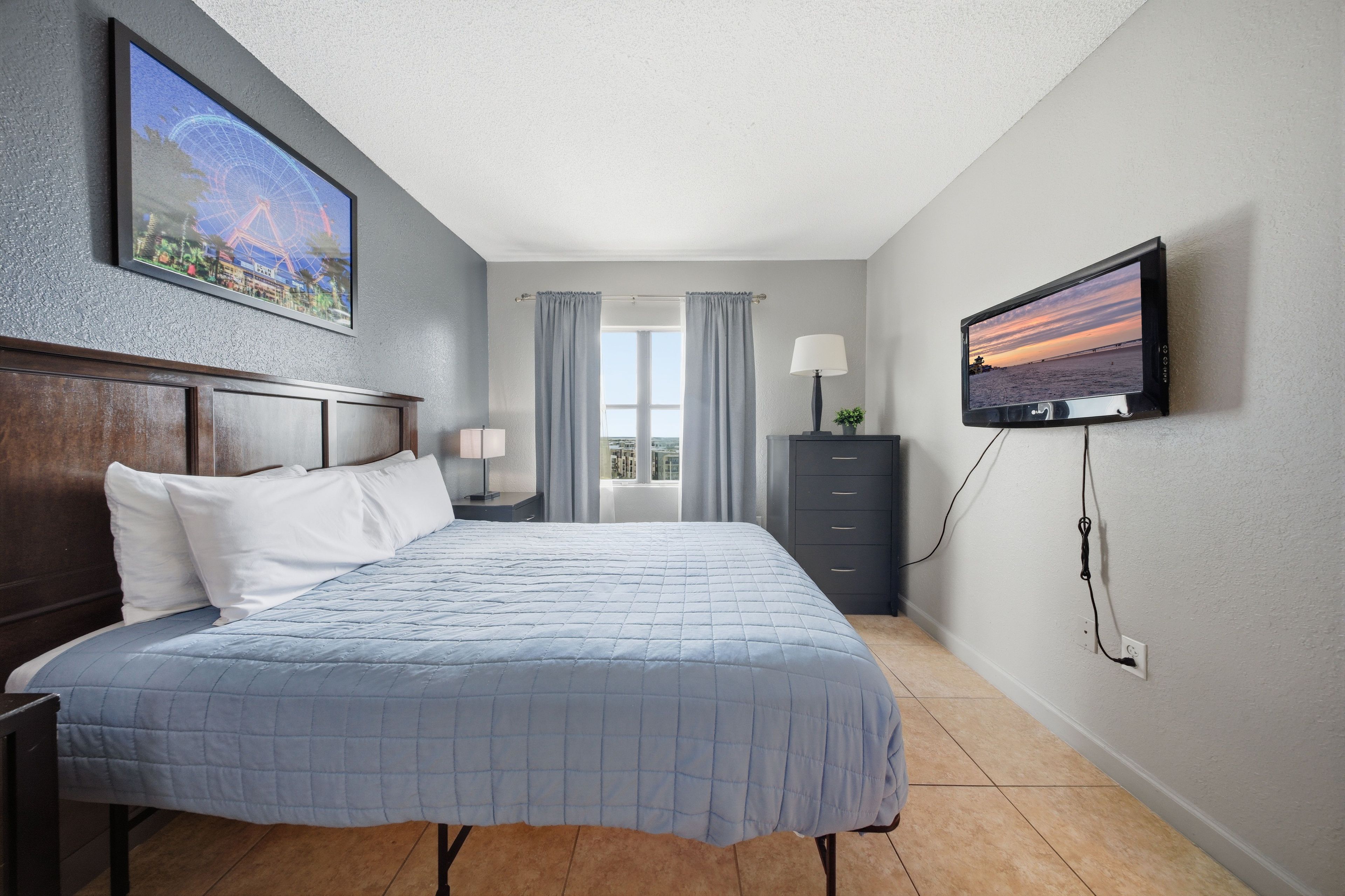 Een hotelkamer met een bed, een televisie, een nachtkastje, een dressoir en een raam met gordijnen.