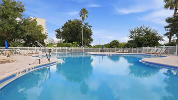 Une piscine entourée d’une clôture blanche, avec des chaises longues et des arbres en arrière-plan.