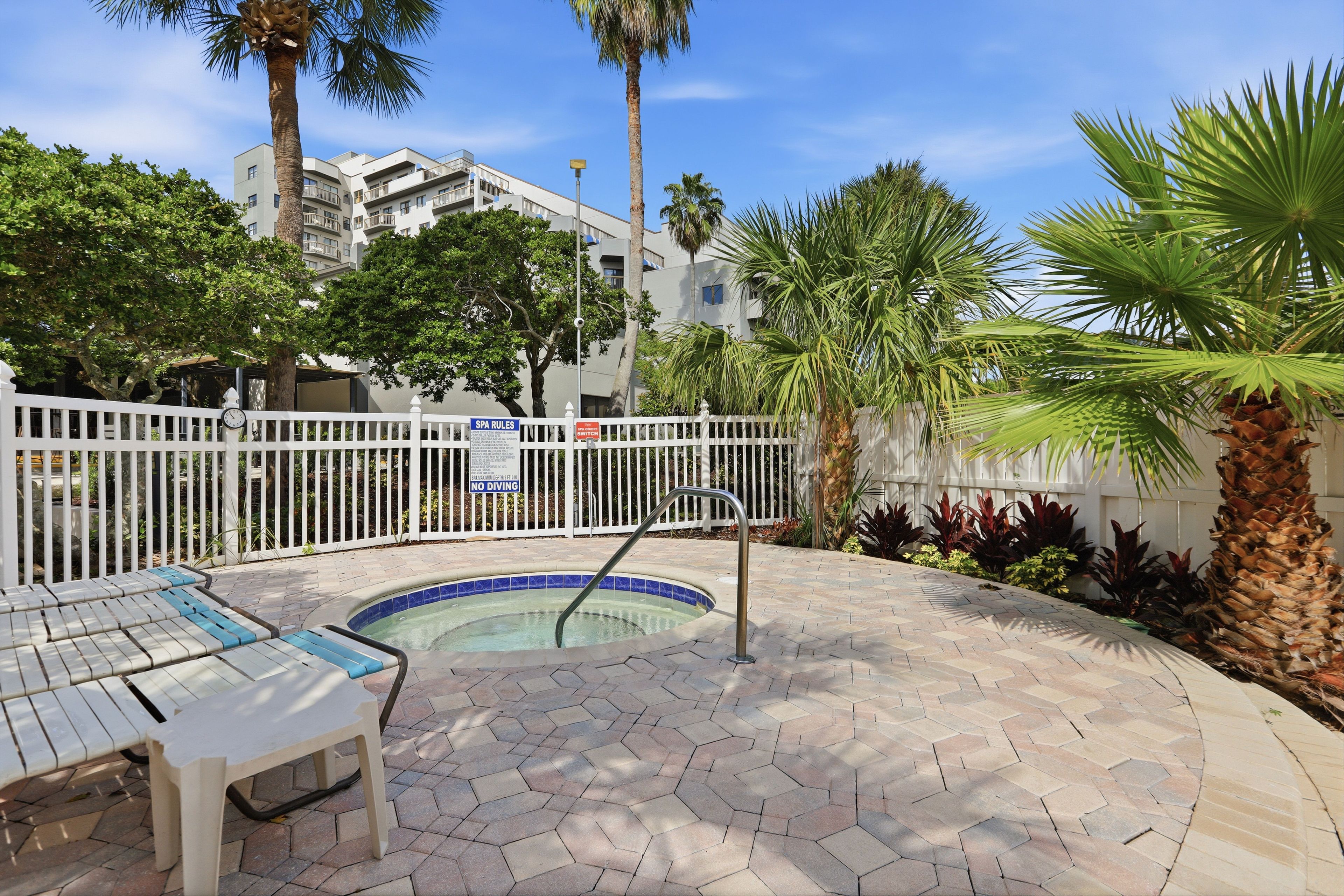 Een zwembadgedeelte met een betegeld terras, ligbedden en een omheining met borden waarop de spa-regels staan.