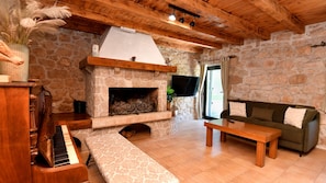 A cozy living room with a stone fireplace, wooden furniture, a piano, and a stone wall.
