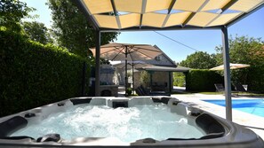 A hot tub with a canopy, a pool, and a stone building in the background.