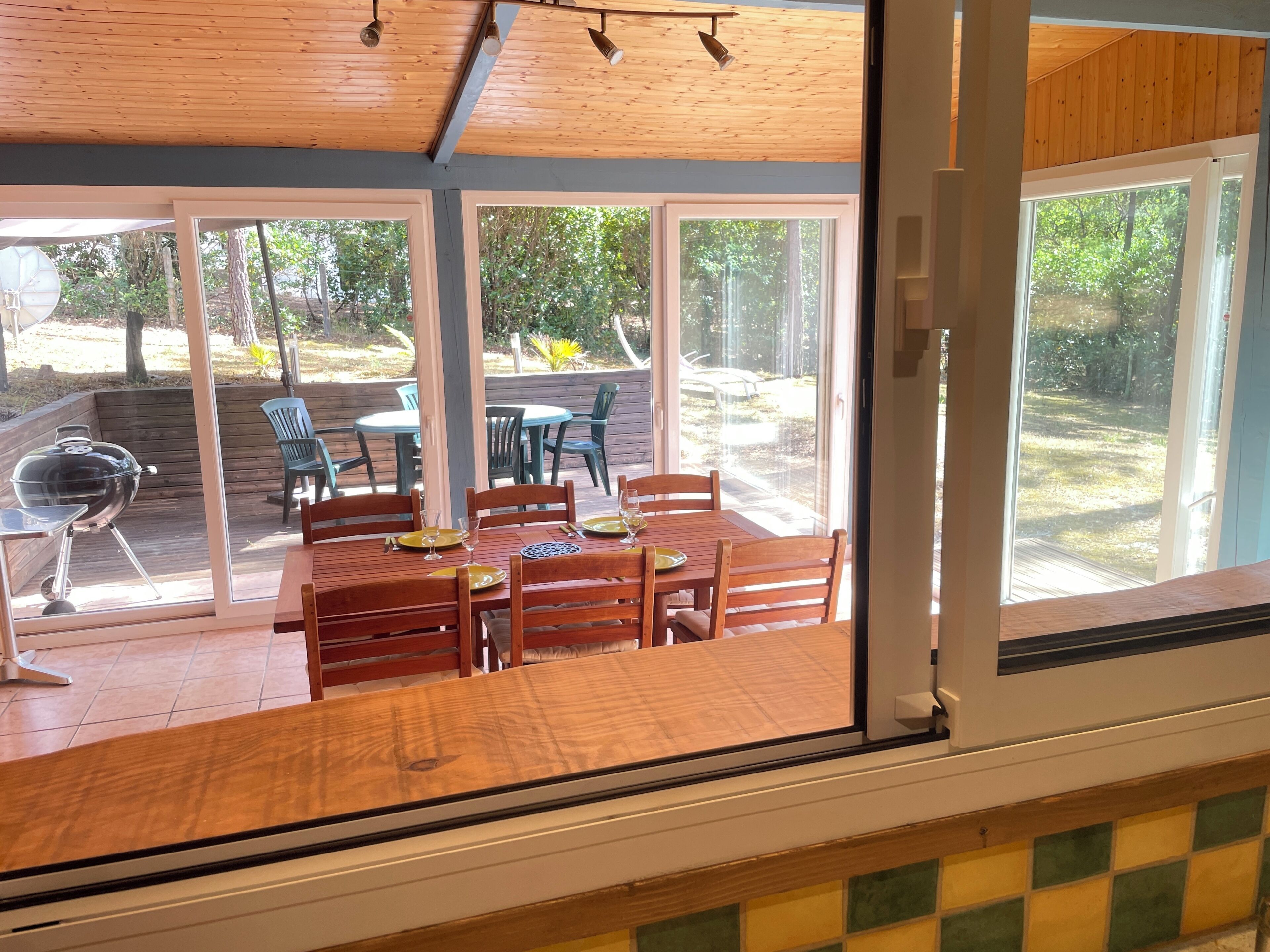 Une terrasse couverte avec une table et des chaises, un barbecue et une vue sur l’extérieur.