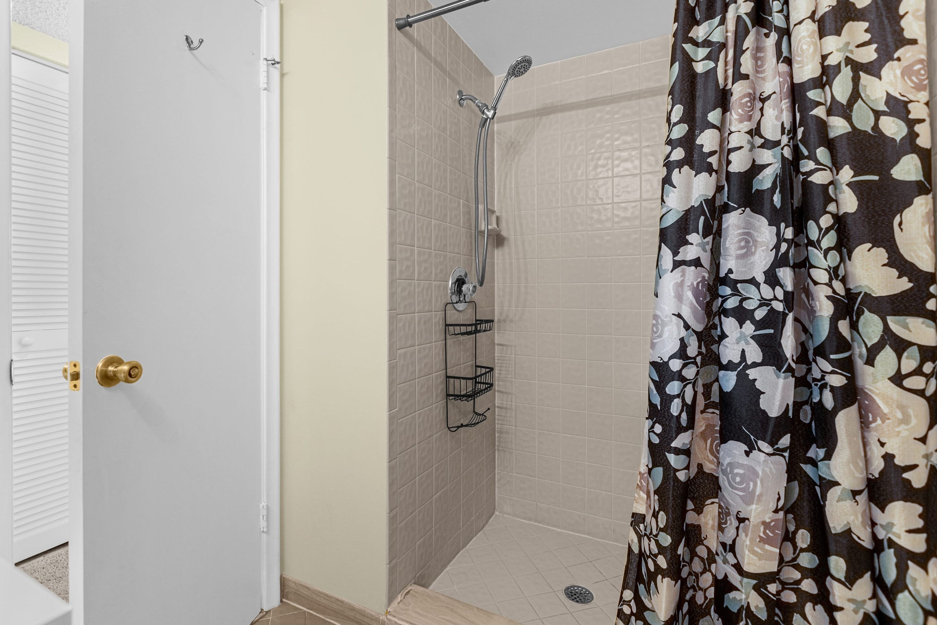 Une douche avec un rideau à motifs floraux, une porte blanche et un mur carrelé.