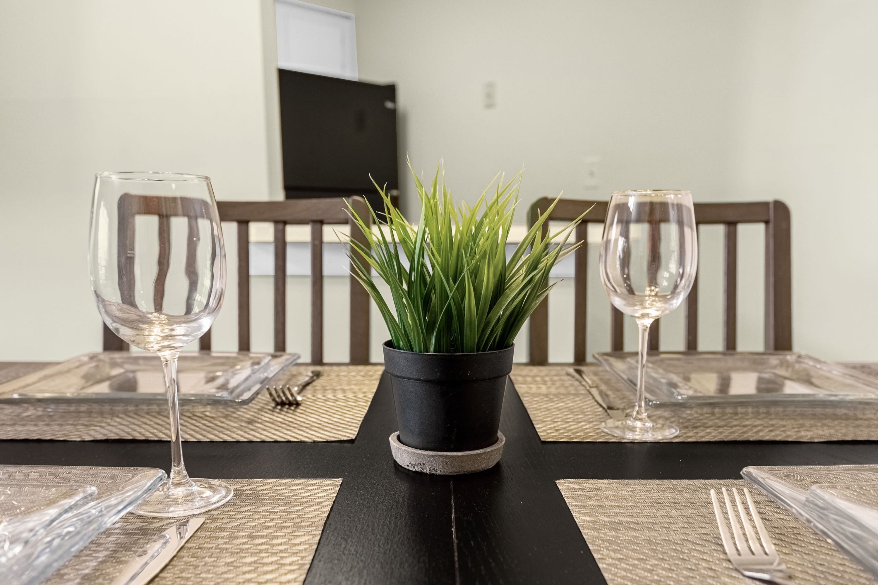 Een eettafel met twee wijnglazen, een potplant en een afstandsbediening aan de muur.