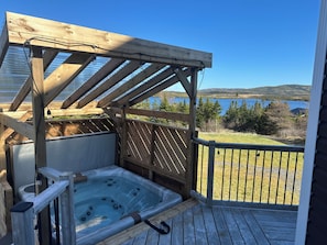 Una terraza de madera con un jacuzzi, una pérgola y vistas a un lago.
