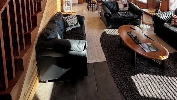 Un amplio espacio habitable con una escalera de madera, un sofá de cuero negro, una mesa de centro de madera y un comedor con mesa y sillas.