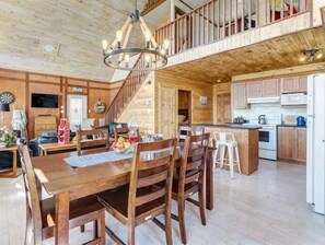 A wooden interior with a dining area, kitchen, and a staircase leading to an upper level. - Rhodies Pondside<br>It's ideal for guests looking to unwind, enjoy scenic views, and experience a quiet getaway. (Placentia Junction)