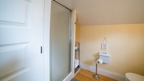 A bathroom with a toilet, a roll of toilet paper, a shelf with towels, and a shower door. - Hayward Field Studio. In the heart of Tracktown USA. (Eugene)
