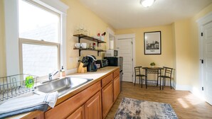A kitchen with wooden cabinets, a stainless steel sink, a microwave, and a dining area with a small table and chairs. - Hayward Field Studio. In the heart of Tracktown USA. (Eugene)