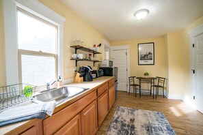 A kitchen with wooden cabinets, a stainless steel sink, a microwave, and a dining area with a small table and chairs. - Hayward Field Studio. In the heart of Tracktown USA. (Eugene)