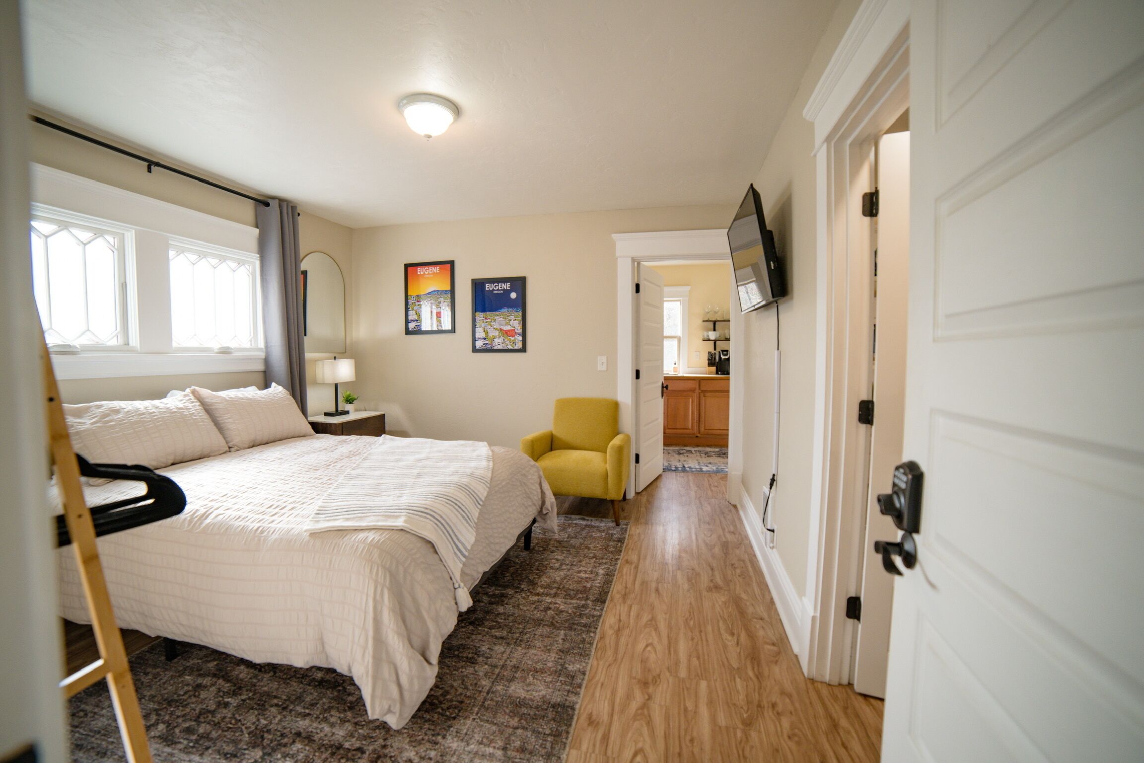 A bedroom with a bed, a chair, a nightstand, a lamp, and a wall-mounted TV.
