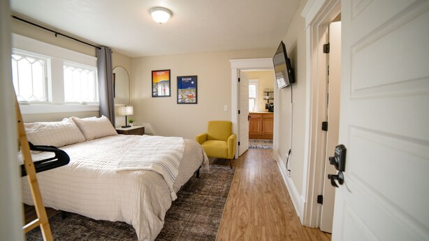 A bedroom with a bed, a chair, a nightstand, a lamp, and a wall-mounted TV. - Hayward Field Studio. In the heart of Tracktown USA. (Eugene)