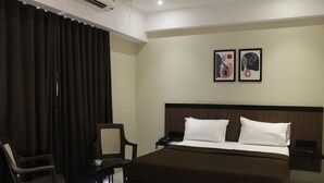 Hotellihuone, jossa on sänky, tuoli, työpöytä ja kaksi kehystettyä kuvaa seinällä.