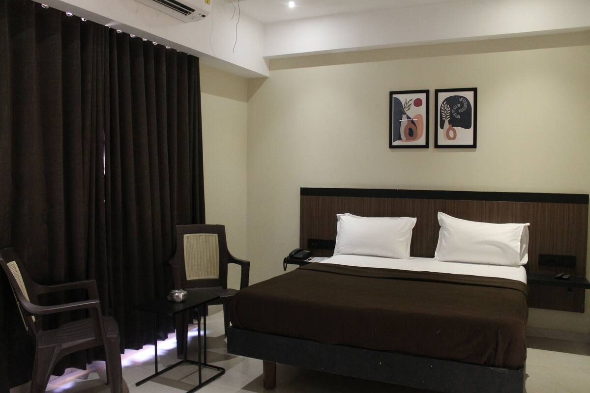 A hotel room with a bed, a chair, a desk, and two framed pictures on the wall.