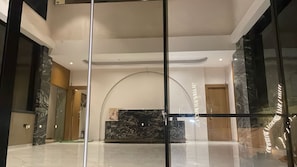 Un vestíbulo moderno con un mostrador de recepción de mármol, separadores de vidrio y un techo alto.