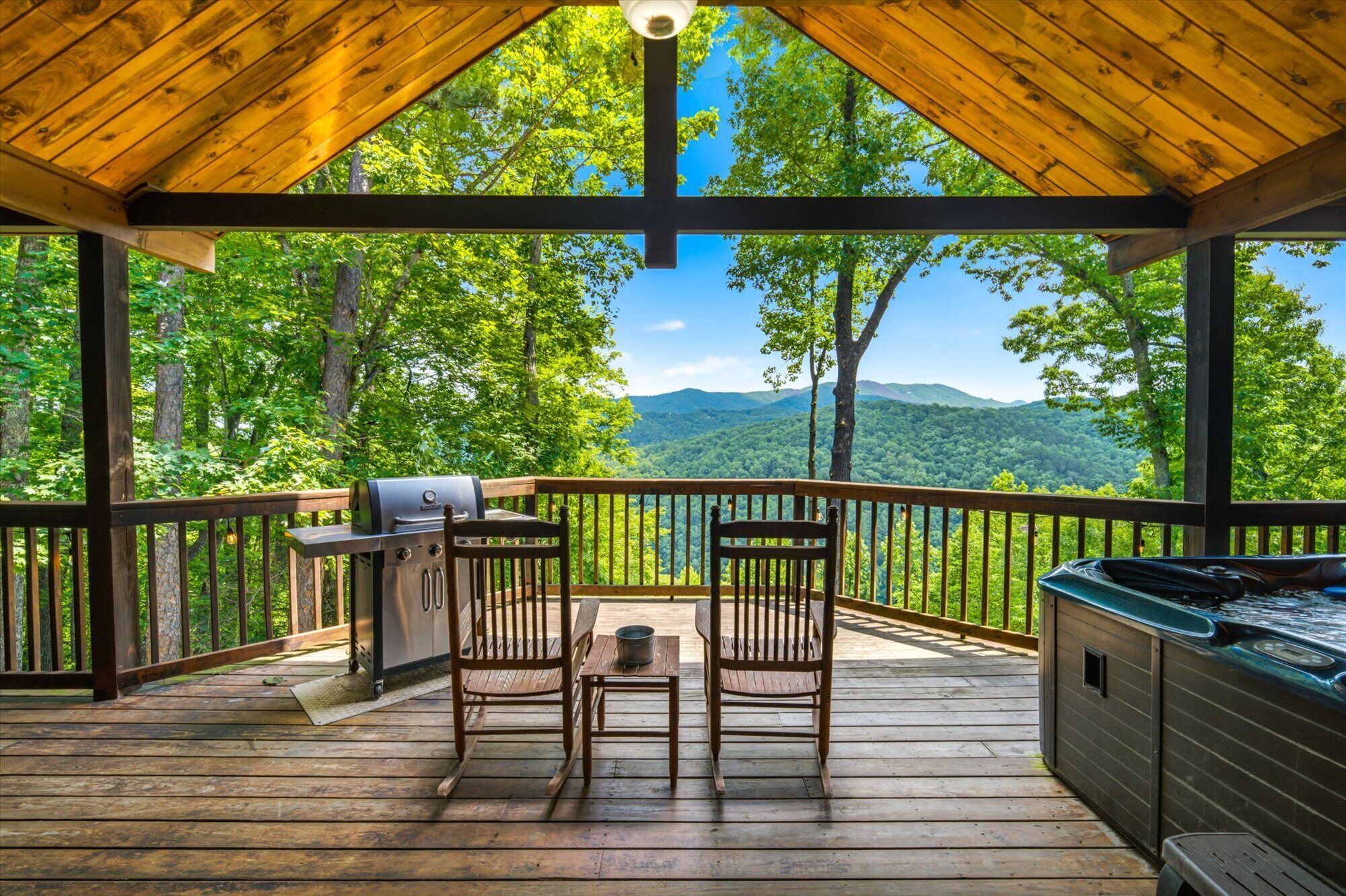 A covered deck with a grill, two chairs, and a hot tub.