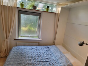 Makuuhuone, jossa on sänky, ikkuna verhoilla, patteri ja seinään kiinnitetty lamppu.