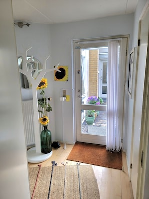 Ein Flur mit einer weißen Tür, die auf einen Balkon mit Topfpflanzen führt.