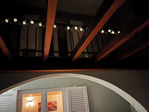 Ein Zimmer mit schrägen Wänden, Holzbalken, einem Fenster mit Rollläden und einer Lichterkette.