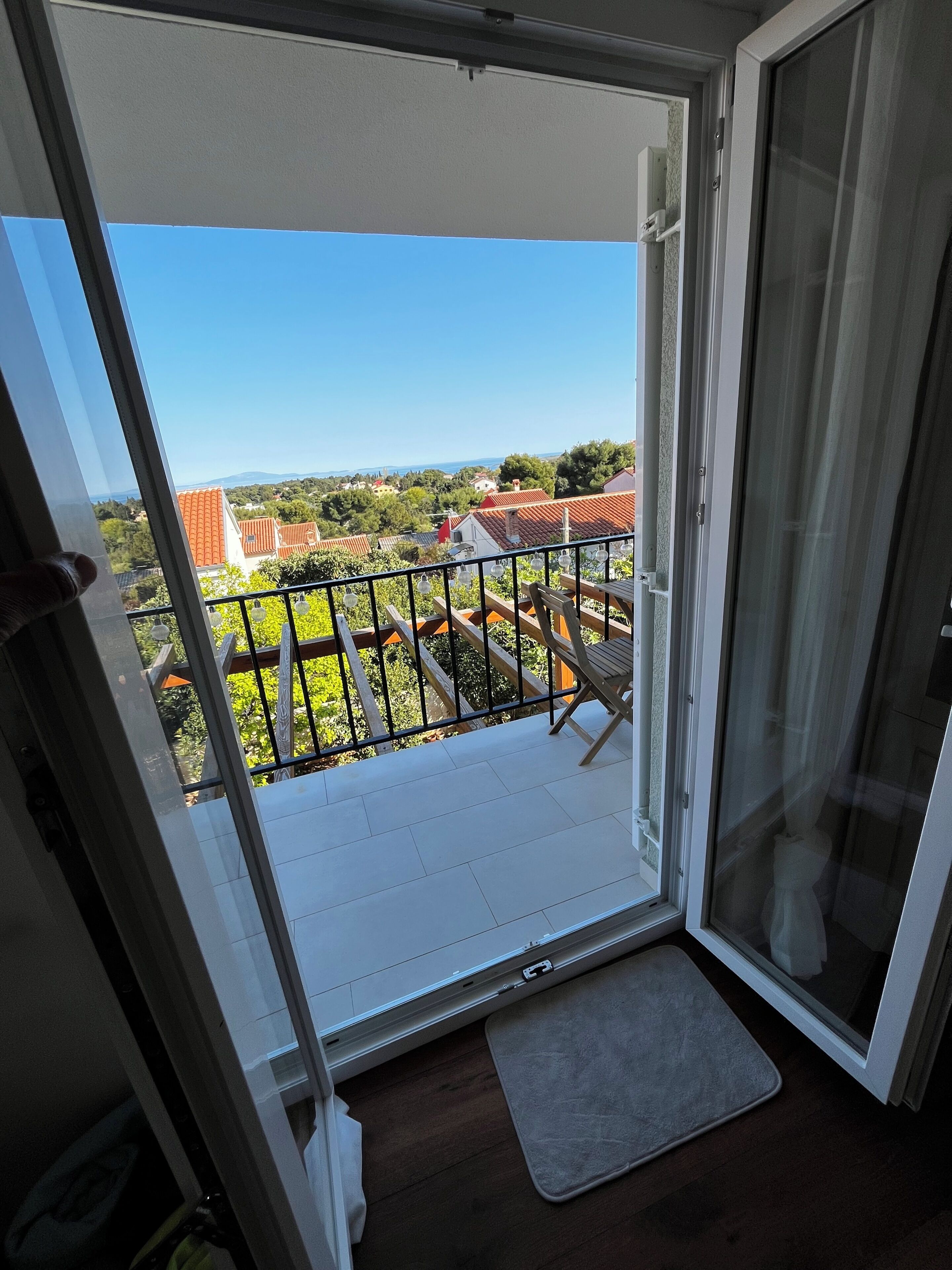 A balcony with a view of a residential area, a wooden chair, and a small mat on the floor.