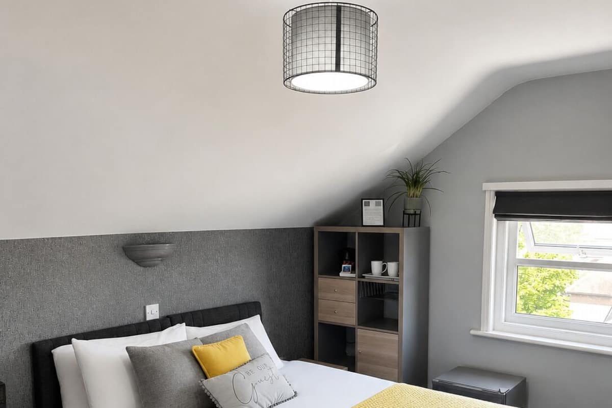 A modern hotel room with a bed, bedside table, nightstand, wardrobe, and a window with a view.
