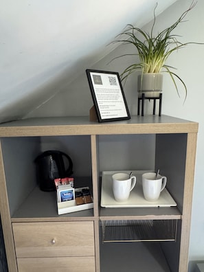 A small wooden cabinet with a framed welcome card, a potted plant, a kettle, and a coffee maker.