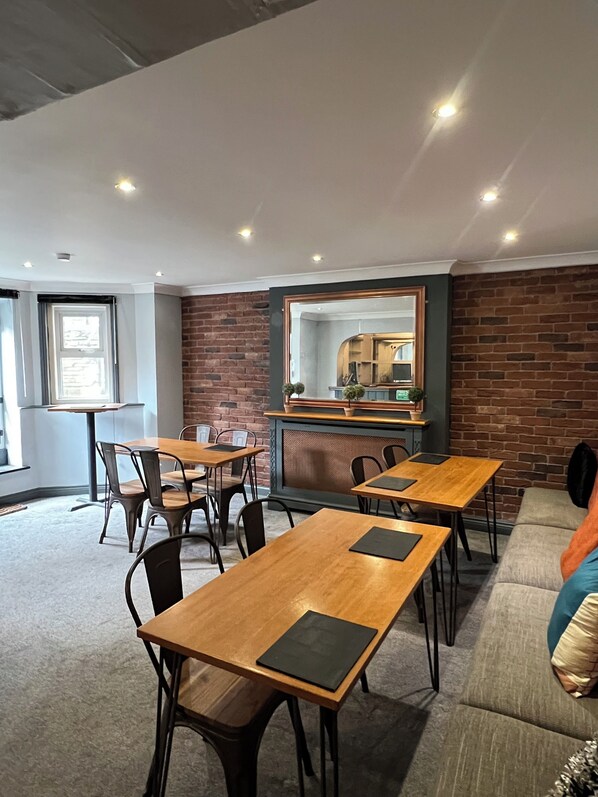 A modern dining area with wooden tables and chairs, a brick accent wall, and a large mirror above the counter.