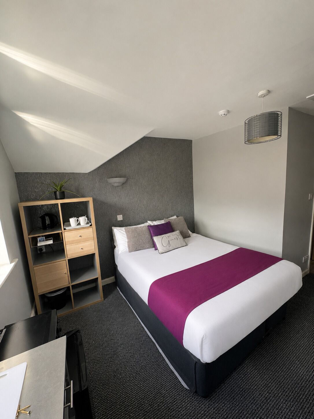 Moderni hotellihuone, jossa on sänky, työpöytä, vaatekaappi ja pieni kasvi.