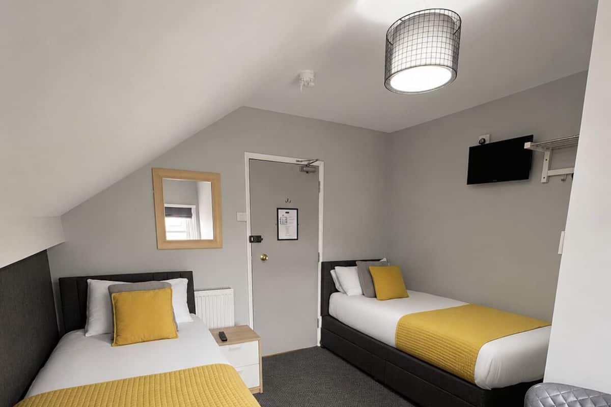 A hotel room with two beds, a desk, a chair, a television, and a ceiling light.