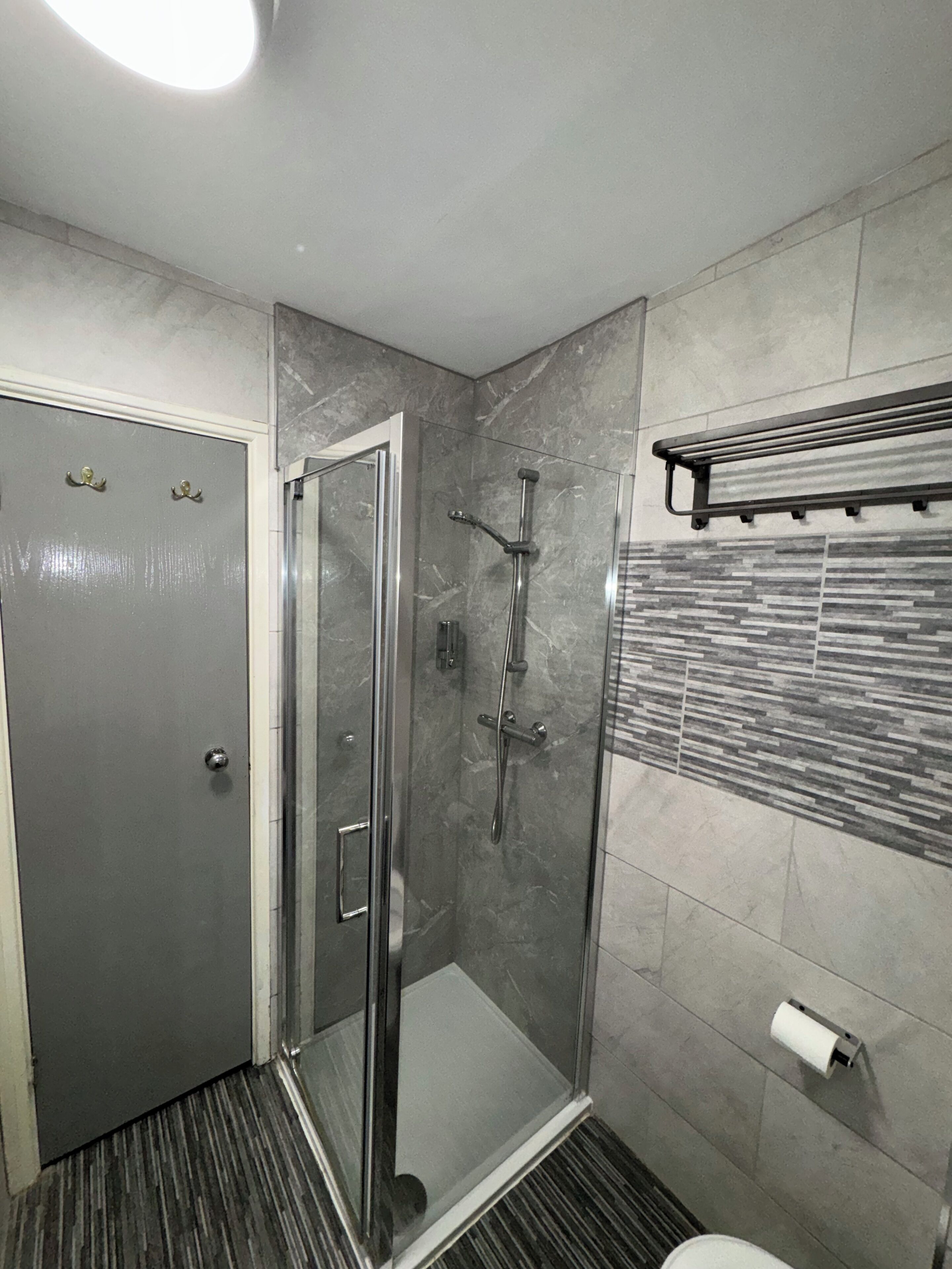 Et moderne badeværelse med en brusekabine i glas, et toilet med papirhåndklædedispenser og en håndklædeholder.