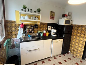 Een kleine keuken met een magnetron, koffiezetapparaat en een spoelbak. Op een plank boven het aanrecht staan potplanten.