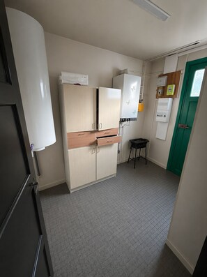 Een kleine keuken met kasten, een koelkast, een wastafel en een groene deur.