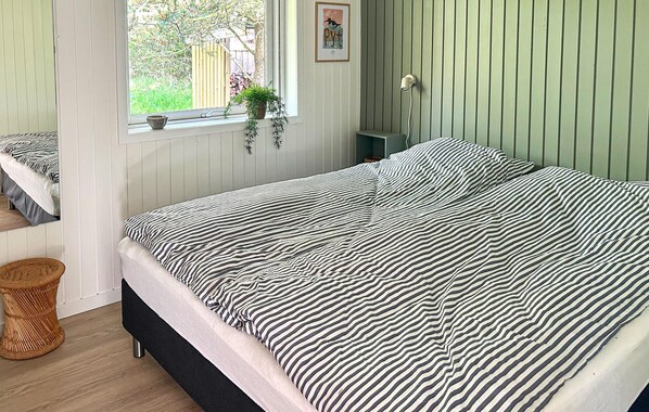 Un dormitorio con cama, ventana con vistas, mesita de noche y lámpara de pared.