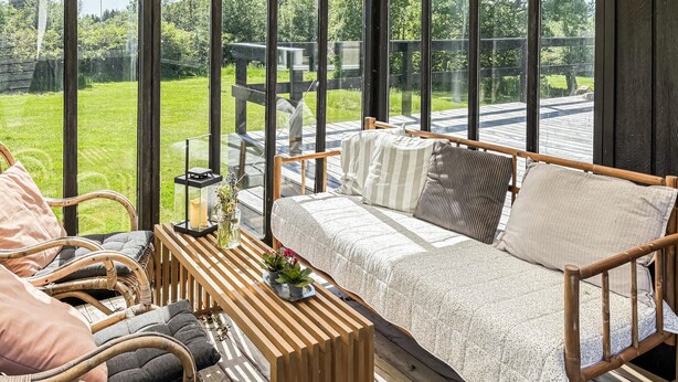 Eine Holzterrasse mit einer Couch und Stühlen, einer Laterne und einer Vase mit Blumen.