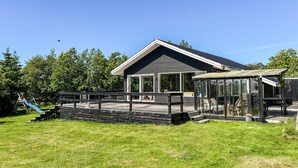 Ein modernes Haus mit einer großen Terrasse, einem überdachten Außenbereich und einer Rutsche im Garten.