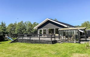 A modern house with a large deck, a covered outdoor area, and a slide in the yard.